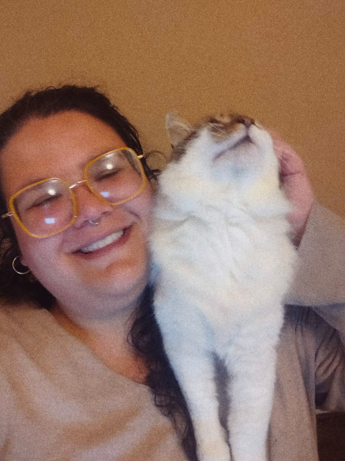 A cat stands on Maia's shoulder, she is smiling and petting it